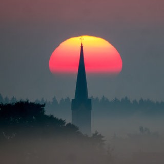 Die Silhouette eines Kirchturms vor der aufgehenden Sonne