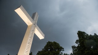 Dunkle Wolken ziehen über einem Kreuz auf.