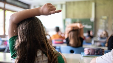 Schülerinnen und Schüler einer vierten Klasse einer Grundschule nehmen am Unterricht teil, während sich eine Schülerin meldet.