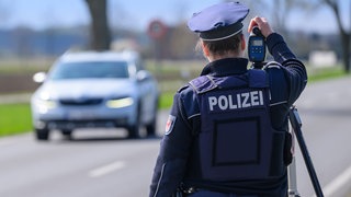 Eine Polizeibeamtin steht mit einem Lasermessgerät an einer Bundesstraße 
