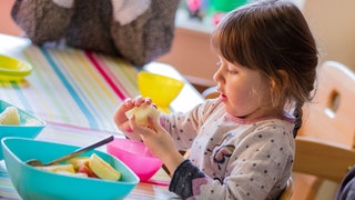 Die kleine Marlene isst in der Kindertagespflegeeinrichtung "Mausekind & Hase" zum Frühstück ein Apfelstück.