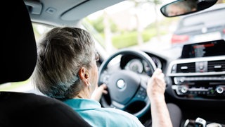 Eine über 90-jährige Frau sitzt hinter dem Lenkrad eines Autos.