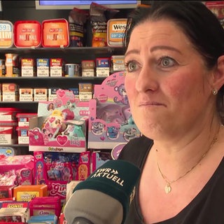 Frau steht in einem Shop vor einem Zigarettenregal und wird interviewt