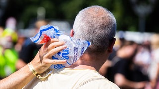 Ein Mann steht in der Sonne, mit einem kühlendem Eisbeutel am Nacken.