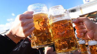 Zwei Hände, die mit gefüllten Bierkrügen anstoßen. (Symbolbild)