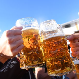 Zwei Hände, die mit gefüllten Bierkrügen anstoßen. (Symbolbild)