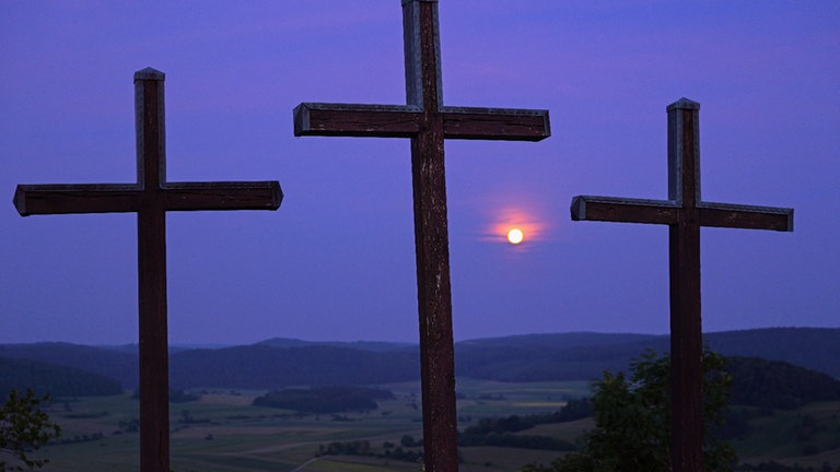 Der Erdbeermond scheint zwischen Holzkreuzen hindurch.