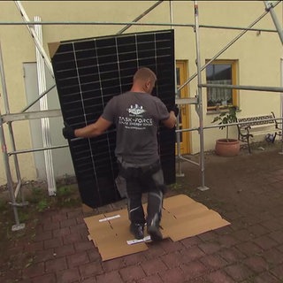 Ein Mann trägt ein Solarpanel zu einem Gerüst