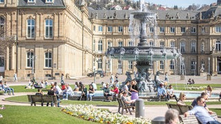 Menschen sitzen auf dem Stuttgarter Schlossplatz auf Bänken in der Sonne. 