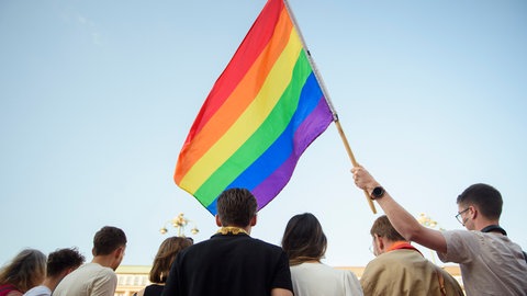 Menschen halten eine Regenbogenfahne in die Höhe.