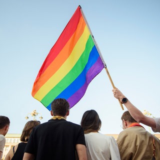 Menschen halten eine Regenbogenfahne in die Höhe.