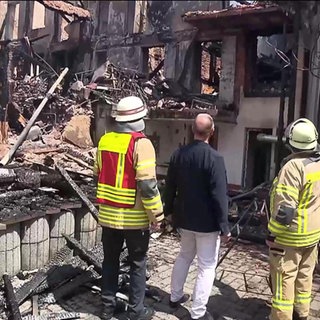 Feuerwehrmänner stehen vor einem abgebrannten Haus