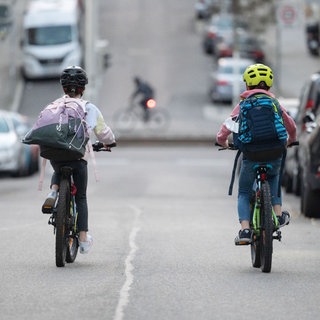 Zwei Schulkinder fahren mit ihren Fahrrädern eine Straße entlang.