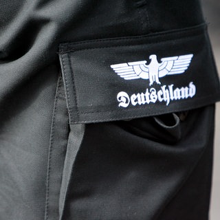Ein Mann trägt eine schwarze Cargo-Hose, auf deren Tasche ein Reichsadler und der Schriftzug Deutschland aufgedruckt sind (Symbolbild).