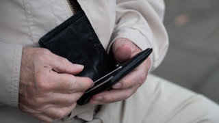 Ein Rentner hält sein Portemonnaie in der Hand. 