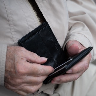 Ein Rentner hält sein Portemonnaie in der Hand. 