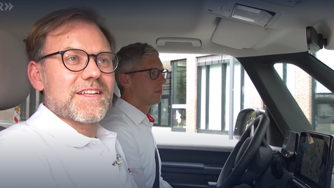 Ein Mann mit Bart und Brille schaut aus dem Beifahrerfenster eines Autos und lächelt