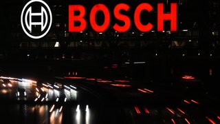 Autos fahren auf unter einem Parkhaus der Messe Stuttgart, auf dem ein Bosch-Logo zu sehen ist. (