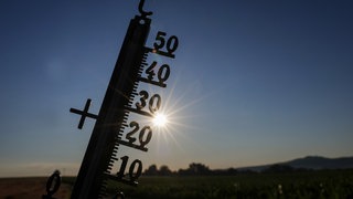 Die Sonne scheint hinter einem Thermometer. Für den Tag werden Temperaturen über 30 Grad vorhergesagt.