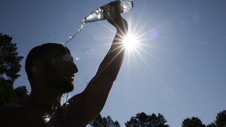 Ein Mann kühlt sich bei sommerlichen Temperaturen ab, in dem er sich eine Flasche mit Wasser über den Kopf schüttet.