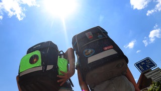 Zwei Kinder laufen mit ihren Büchertaschen im Sonnenschein.