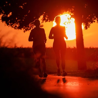 Zwei Frauen joggen, während hinter ihnen die rote Sonne aufgeht. Am Mittwoch erwartet der Deutsche Wetterdienst den Höhepunkt der Hitzewelle in Baden-Württemberg. Die Temperaturen erreichen bis zu 40 Grad.