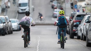 Zwei Schulkinder fahren mit ihren Fahrrädern eine Straße entlang. Schulstraßen ohne Elterntaxis könnten für mehr Sicherheit sorgen.