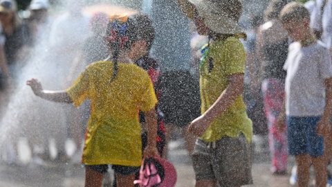 Kinder kühlen sich an einem Wassersprenger ab.
