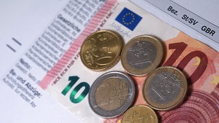 Euro- und Centmünzen liegen auf einer Entgeltabrechnung. Der Mindestlohn in Deutschland steigt bis 2027 auf 14, 60 Euro.