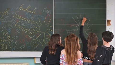Kinder malen an einer Schultafel mit der Aufschrift "Endlich Sommerferien"