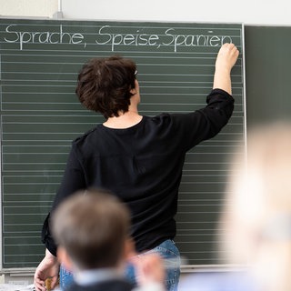 Symbolbild: Eine Lehrerin schreibt in einer Schule Worte an eine Tafel.