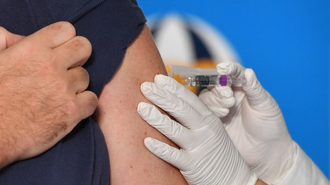 Eine Ärztin impft einen Patienten in den Oberarm. Gegen das Chikungunya-Virus gibt es seit 2025 auch eine Totimpfung. Eine Impfung wird Erwachsenen emfohlen, die eine Reise in die Tropen planen.