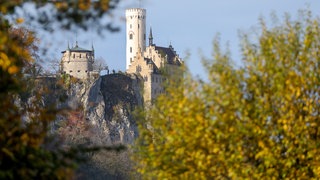 Blick durch herbstlich verfärbtes Laub auf das Schloss Lichtenstein auf der Schwäbischen Alb. 