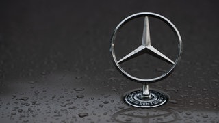 Regentropfen sind auf einem Mercedes-Stern auf einem Fahrzeug zu sehen (Symbolbild).
