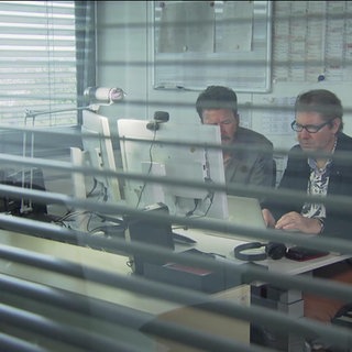 2 Männer sitzen in einem Büro an einem Computer