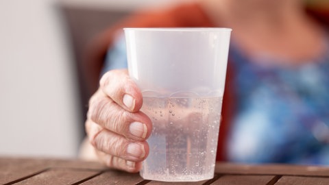 Die Bewohnerin eines Seniorenzentrums hält einen Becher mit Wasser. 