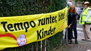 Ein Spannband mit der Aufschrift "Tempo runter, bitte! Kinder" wird an einem Schulweg gespannt. Kontrollen der Polizei vor Schulen und Kindergärten haben gezeigt: Oft gefährden Autofahrer mit ihrer Fahrweise Kinder.