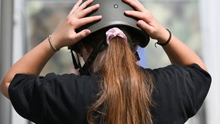 Archiv: Eine junge Frau setzt sich auf dem Gelände der Sonderschau der Bundeswehr einen Helm auf.