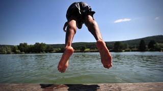 Ein junger Mann springt mit Kopfsprung in einen Badesee.