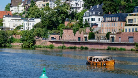Ein Boot fährt auf dem Neckar an Villen der Innenstadt vorbei.