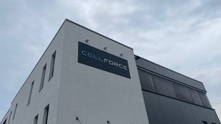 Ein schlichtes Fabrikgebäude in grau und weiß vor bewölktem Himmel. In futuristischer Schrift steht darauf das Wort "Cellforce"
