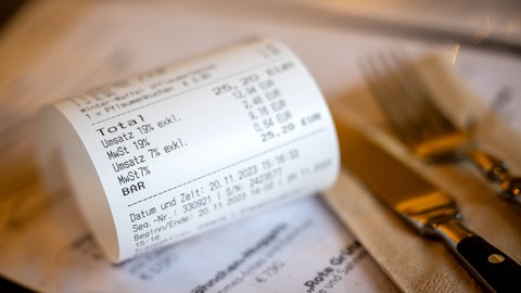 Eine Rechnung mit Umsatzsteuer und Mehrwertsteuer liegt auf der Speisekarte eines Restaurants. Durch die Abschaffung der Bonpflicht könnte Steuerhinterziehung in der Gastronomie leichter werden.