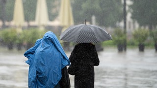 Spaziergänger schützen sich mit Jacke und Schirm vor Regen. In Rheinland-Pfalz wird das Sommerwetter der vergangenen Tage durch Schauer, Gewitter und Starkregen abgelöst.