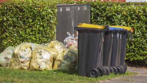 In einem Vorgarten stehen Gelbesäcke und volle Mülltonnen: In Baden-Württemberg gibt es pro Jahr mehrer Tausend NAchbarschaftsstreit. Oft muss die Polizei wegen Kleinigkeiten anrücken.