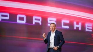 Porsche-Chef Oliver Blume steht vor einem Porsche-Schriftzug.