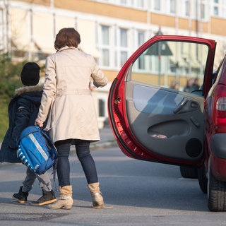 Eine Mama bringt ihr Kind mit dem Auto zur Schule.