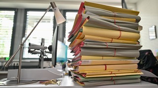Viele Akten stapen sich auf einem Schreibtisch. Durch die Teillegalisierung von Cannabis mussten in Baden-Württemberg 25.000 Fälle noch einmal geprüft werden.