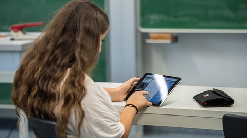 Eine Schülerin arbeitet in einem Klassenzimmer an einem Tablet. Ab dem Schuljahr 202526 führt Baden-Württemberg zunächst für alle 5. und 6. Klassen das neue Fach "Informatik und Medienbildung" ein.