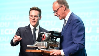 Beim Landesparteitag der BW-CDU überreichte Manuel Hagel Bundeskanzler Friedrich Merz noch ein Modell eines Porsche-Motors. Nun fordert Hagel von Merz Klartext in Bezug auf das geplante Verbrenner-Aus.