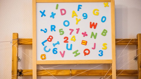 Eine Tafel mit Buchstaben und Zahlen in einer Kita. Kinder aus von Armut betroffenen Familien haben seltener einen Kita-Platz.